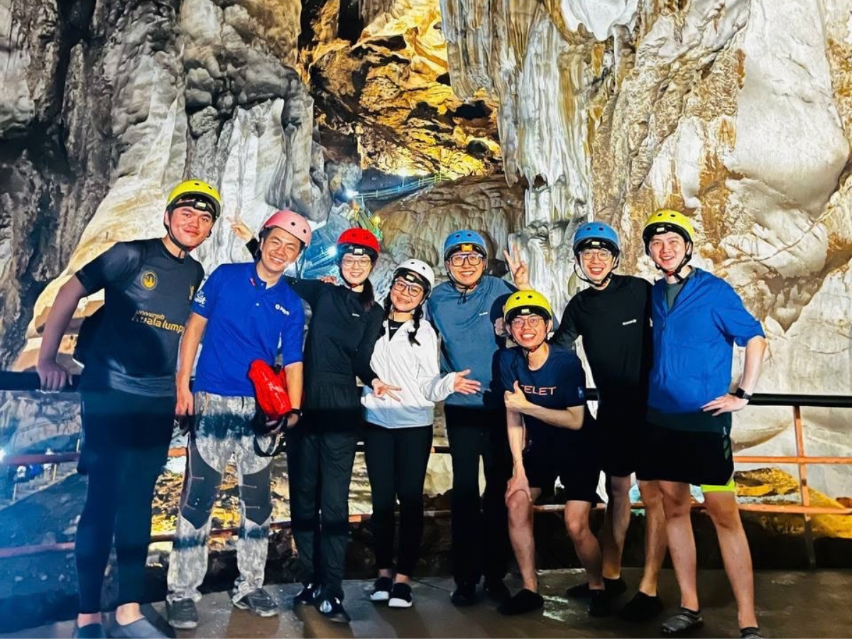 Caving participants in helmets posing among large stalactite formations inside Gua Tempurung