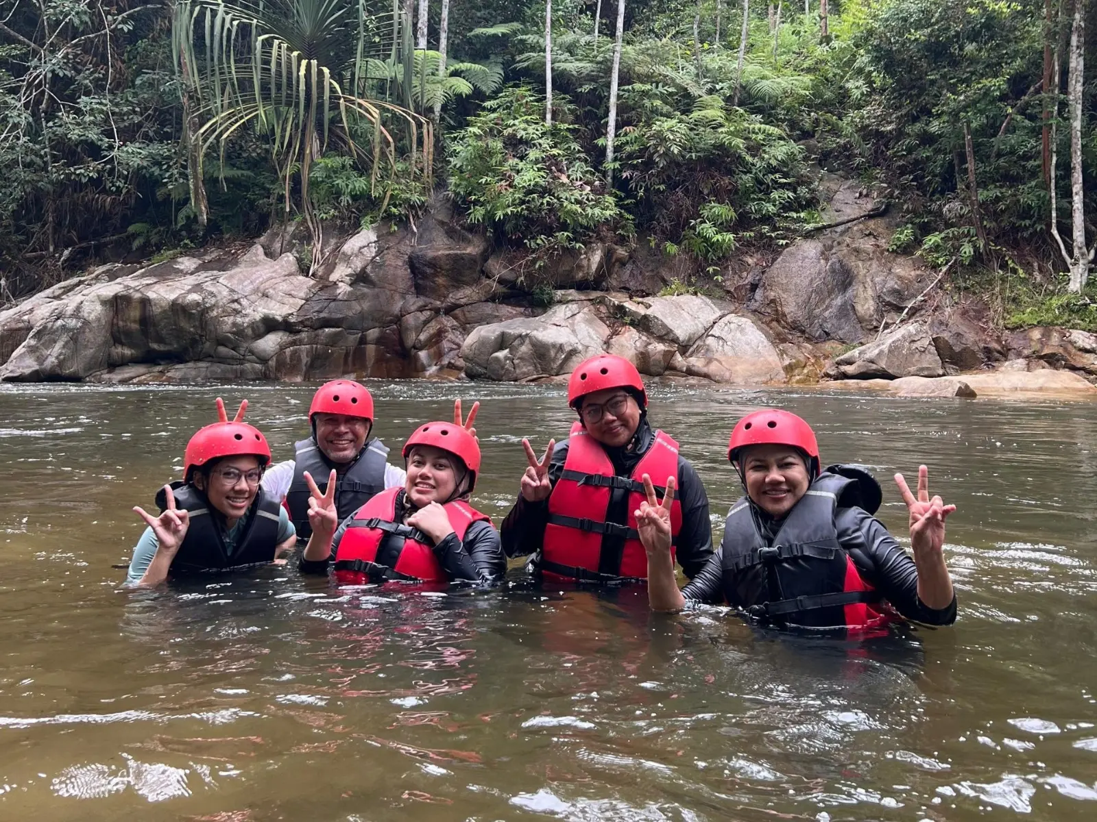 Group of five smiling chest-deep in the river wearing helmets and life jackets